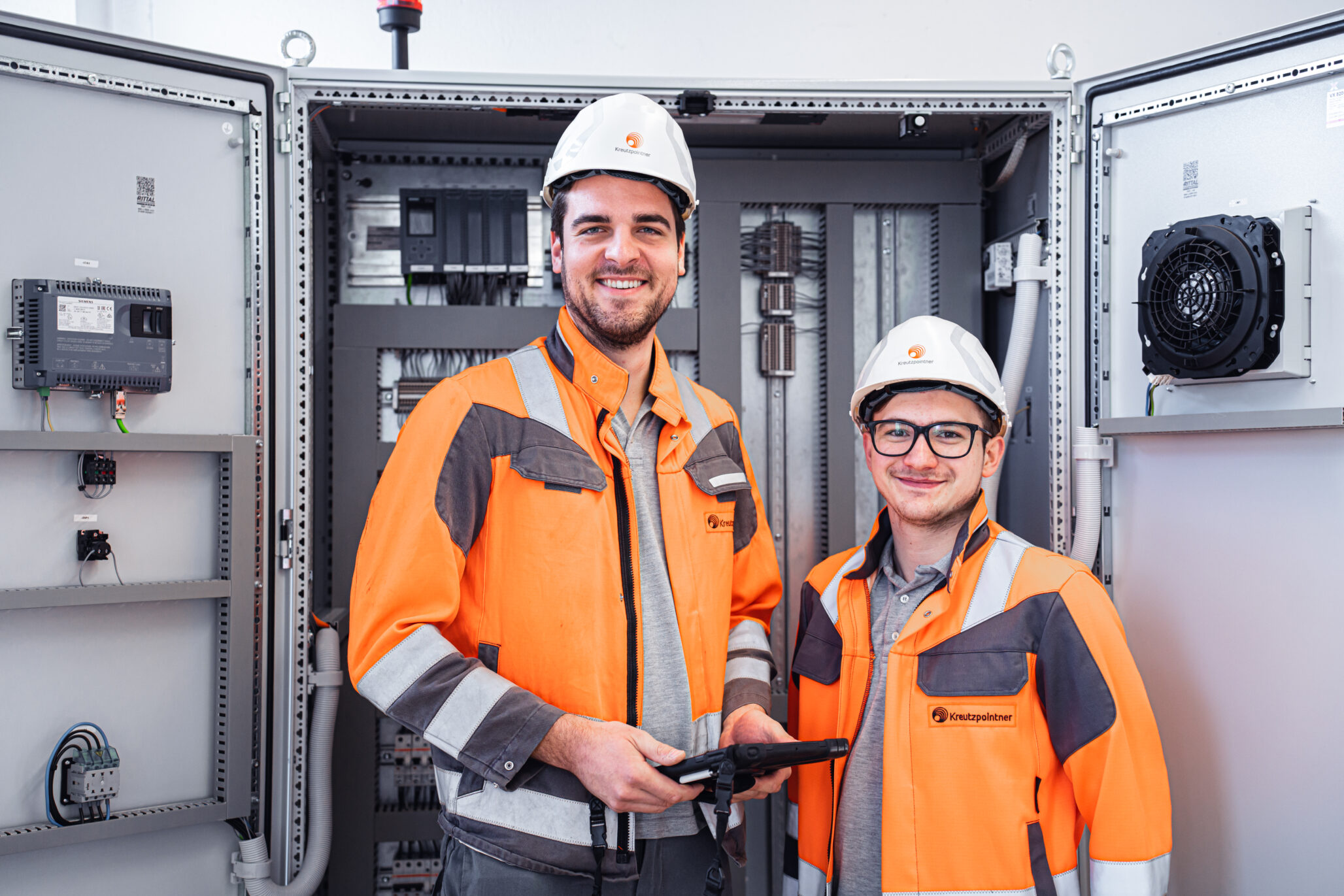 Zwei Fachkräfte in Schutzkleidung arbeiten an elektrischen Anlagen – Kreutzpointner.