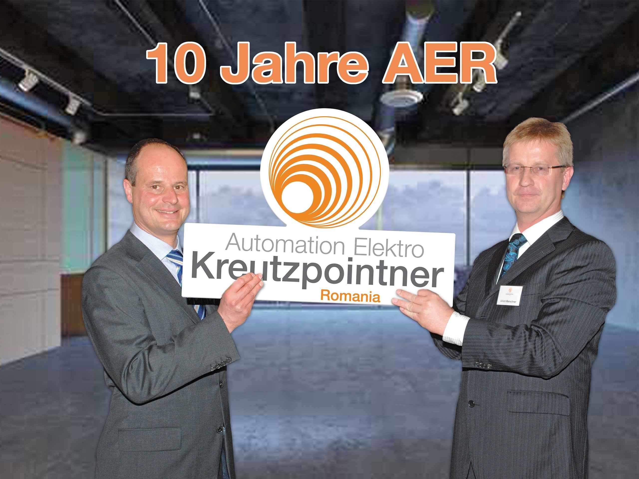 Zwei Männer im Anzug halten gemeinsam ein Schild mit der Aufschrift „10 Jahre AER Kreutzpointner“. Beide lächeln in die Kamera.