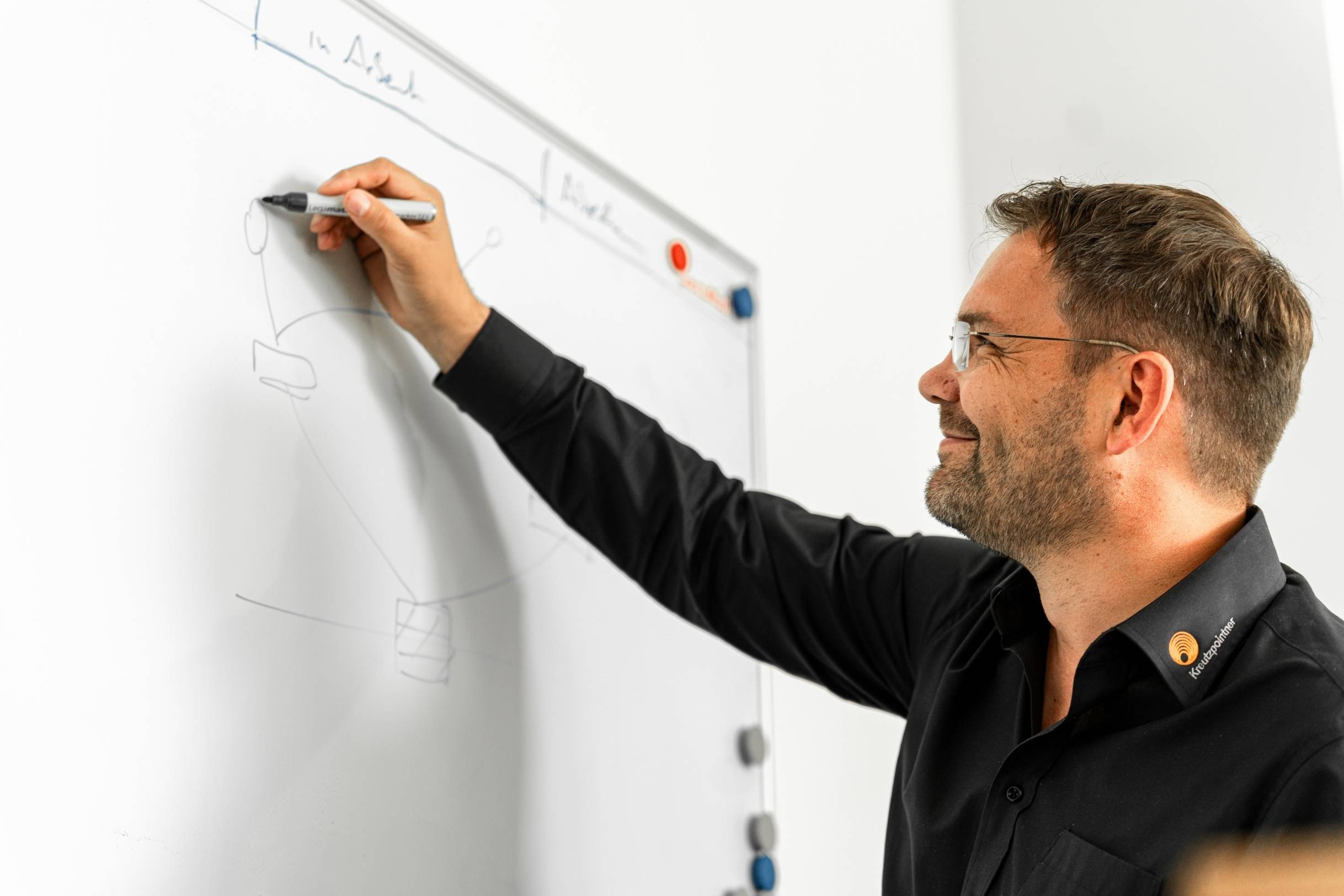 Mann in schwarzem Hemd schreibt an ein Whiteboard.