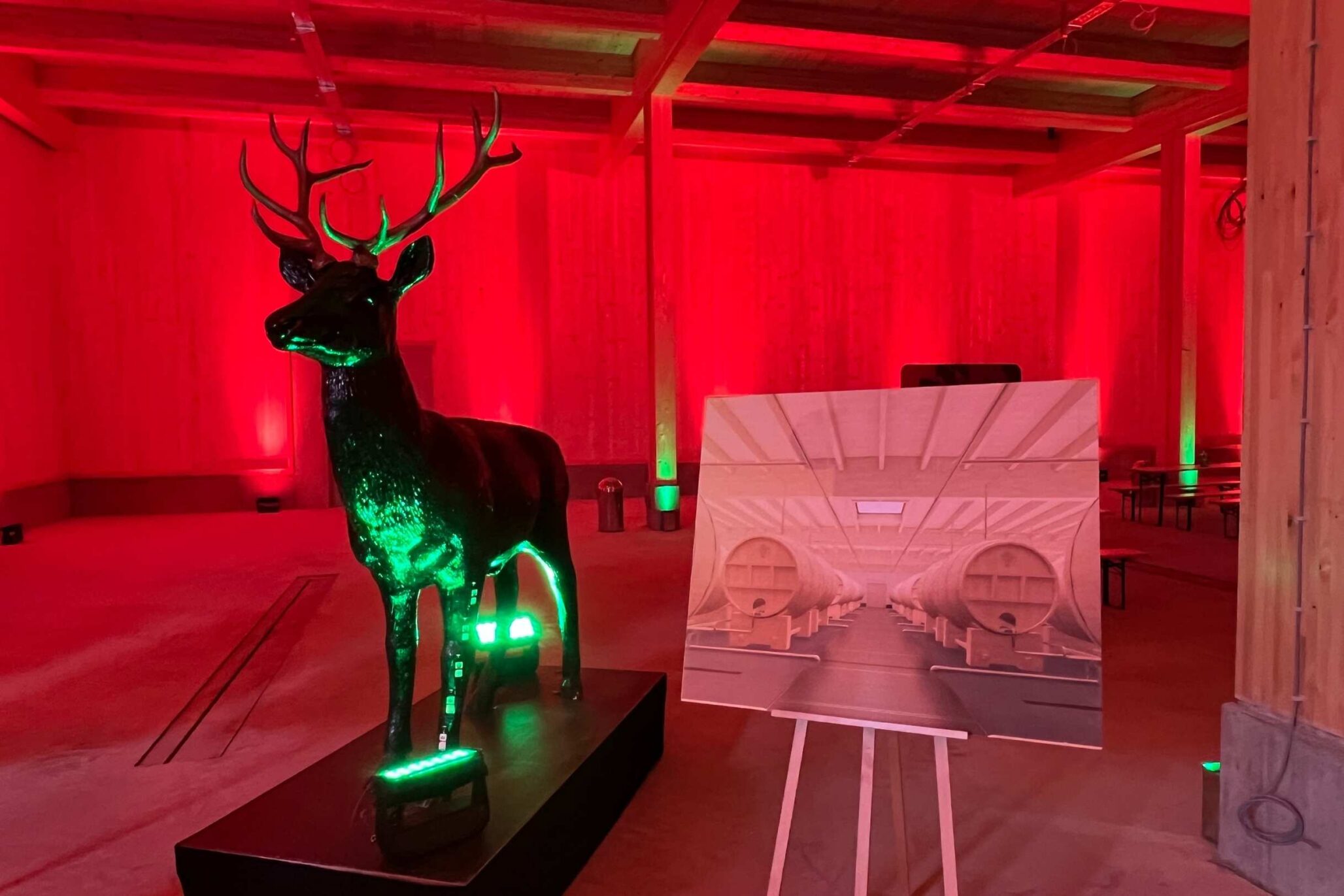 Leuchtend grüner Jägermeister-Hirsch in einer rot ausgeleuchteten Halle des neuen Eichenfass-Lagers, daneben ein Präsentationsplakat.