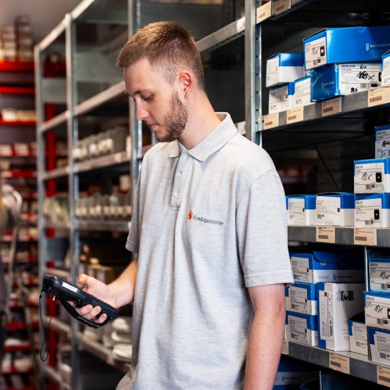 Mitarbeiter im Lager scannt mit einem Handscanner Produkte in einem Regal mit Ersatzteilen.