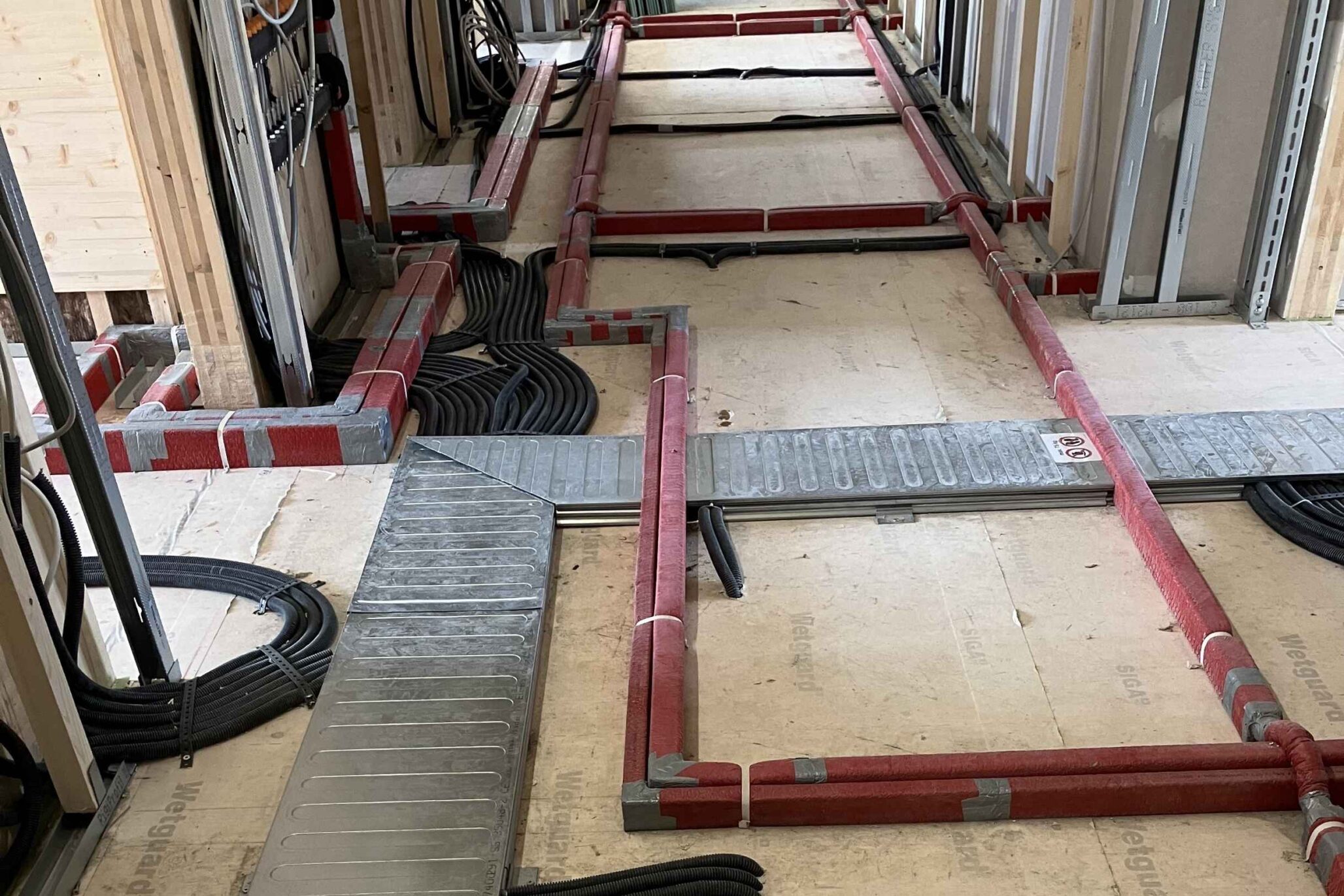 Technische Installation von Kabeltrassen und Versorgungsleitungen auf dem Rohfußboden eines Neubaus.
