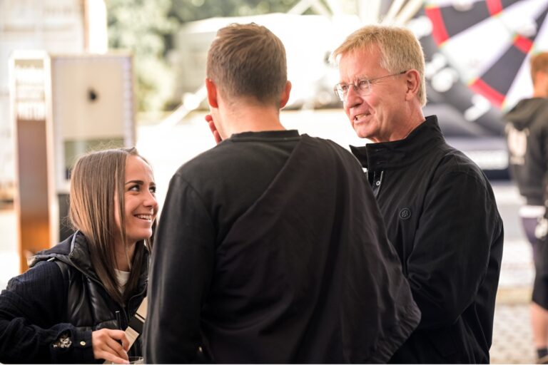 ein Mann unterhält sich mit einer Dame und einem weiteren Herren draußen auf einem Sommerfest