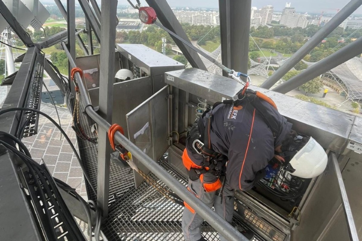 Ein Mann in Arbeitskleidung und Sicherung arbeitet in der Höhe an einer elektrischen Anlage.