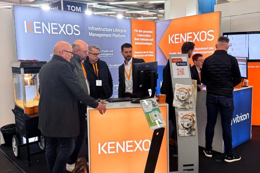 Ein Messe stand mit Messepersonal und Besuchern die interessiert auf einen Bildschirm schauen.