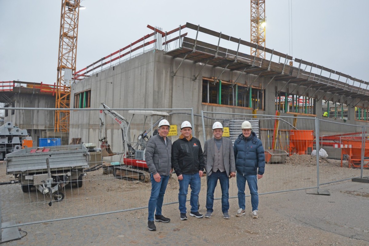 Vier Männer stehen mit Helmen vor einer Baustelle.