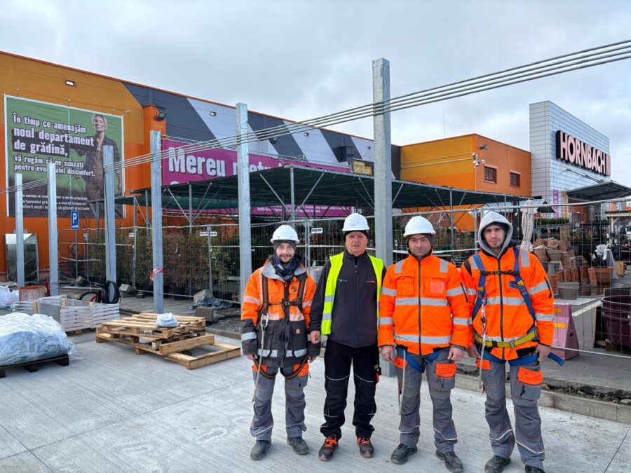 Vier Männer stehen vor einem Gartencenter und tragen Arbeitskleidung und Helme.