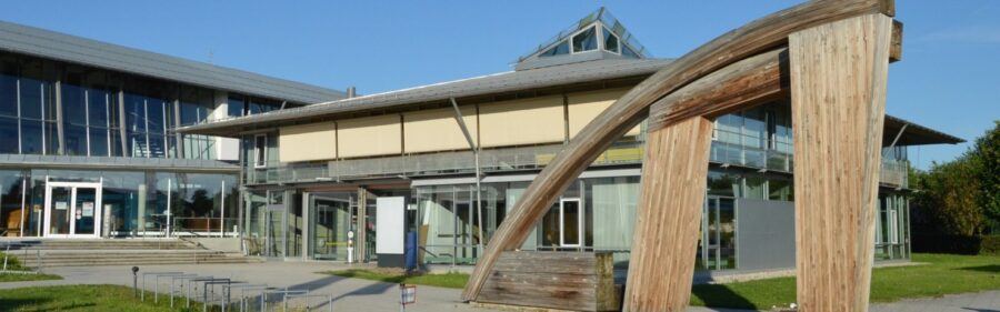 Größeres Bürogebäude mit einer Holz Skulptur im Vordergrund