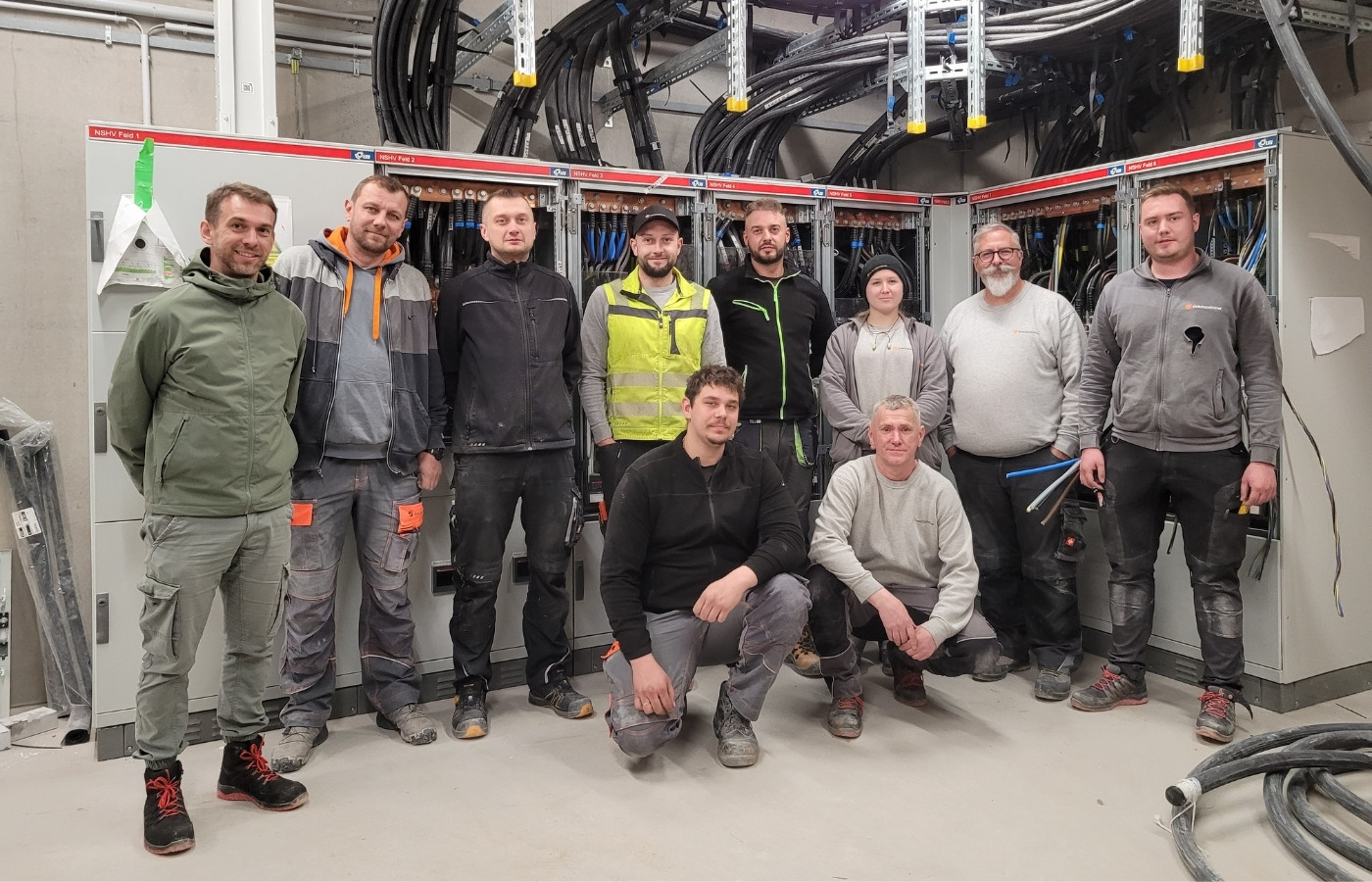 Teamfoto von Männern vor einem Schaltschrank, der ein Projekt in der Arbeit ist.