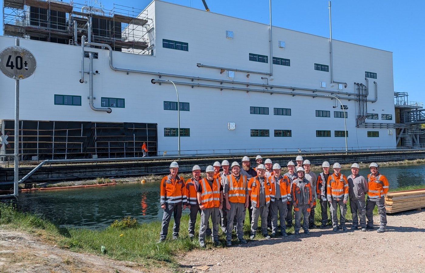 Gruppenfoto von Männern in Arbeitskleidung vor einem Werk, wo davor noch Wasser fließt.