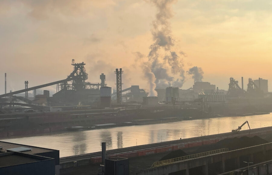 Panoramaaufnahmeines Industriewerks, wo Rauch aufsteigt, bei abendlicher Sonne
