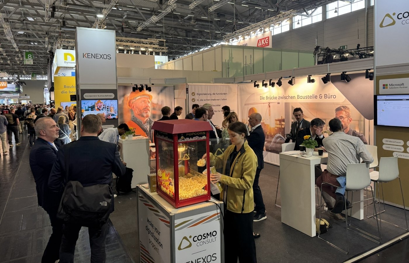 Messestand in einer großen Messehallle, mit vielen Besuchern und einer Popcornmaschine im Vordergrund