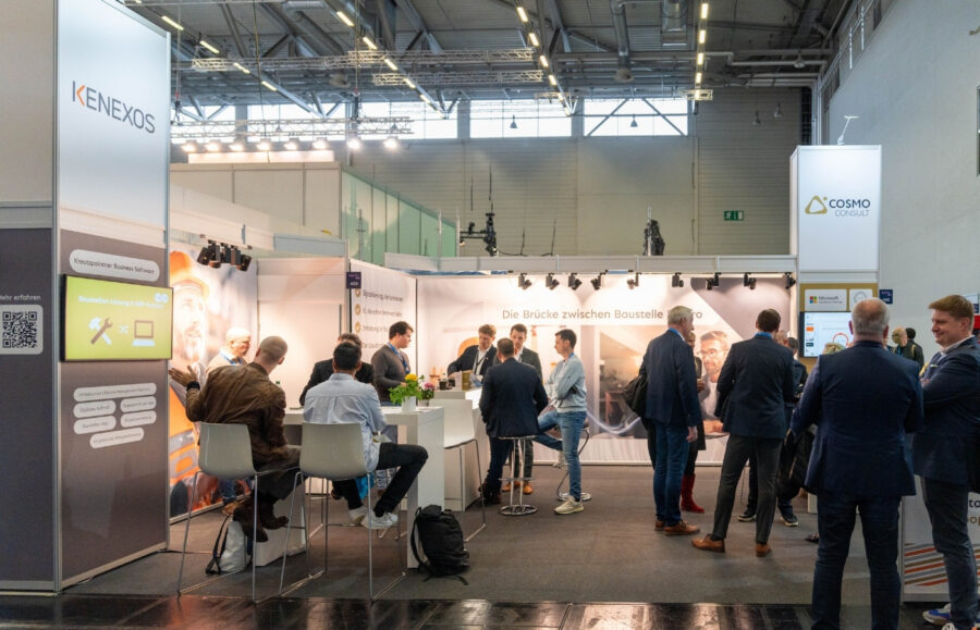 Ein Messestand auf in einer großen Messehalle mit Besuchern am Stand, die sich unterhalten.