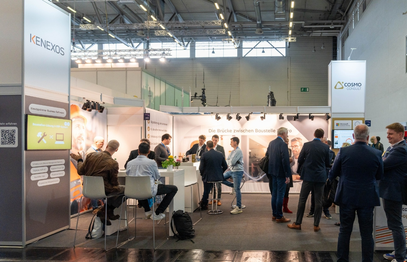 Ein Messestand auf in einer großen Messehalle mit Besuchern am Stand, die sich unterhalten.