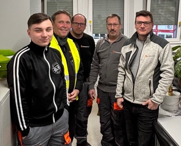 5 Herren stehen in einem kleinen Büro und lachen in die Kamera.