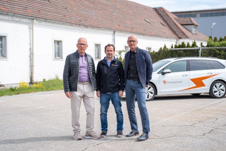 Drei Herren stehen vor einem Fahrzeug und einem Gebäude im Hintergrund.