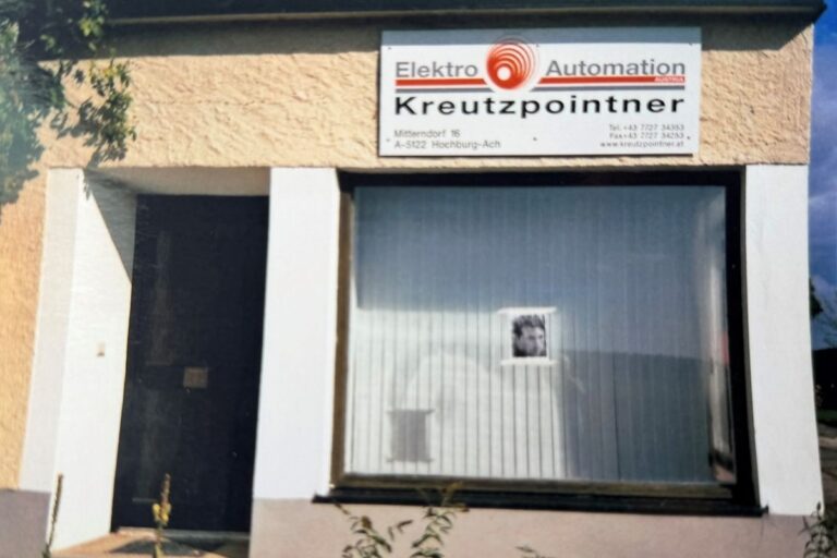 Eine ältere Aufnahme eines Gebäudes mit einem großen Fenster, daneben eine Tür und obendrüber ein großes weißes Schild.